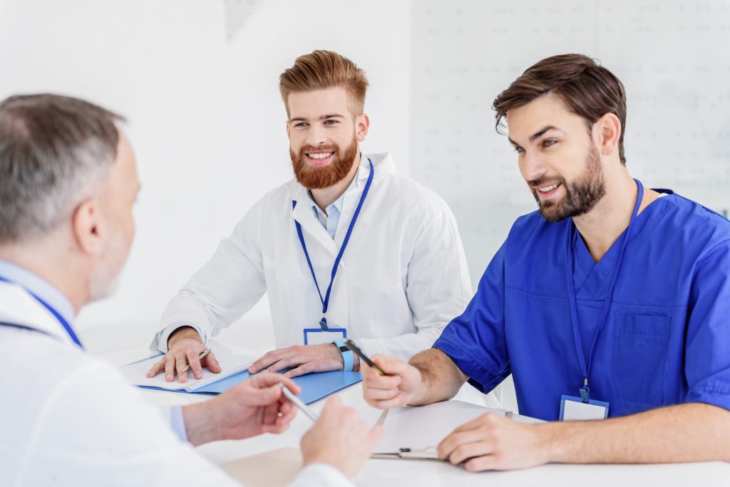 Two young medical workers are listening to senior doctor with attention. They are making notes and smiling